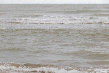 Photo of the sea with small waves, seen from an angle at eye level. The water is gray and slightly brown in color