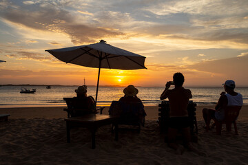 Silhueta de pessoas na praia olhando e fotografando o pôr-do-sol durante o entardecer em uma praia do nordeste brasileiro