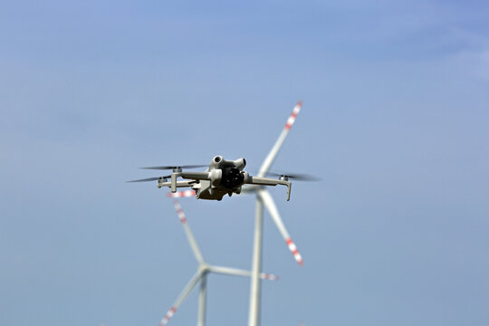 Dron w powietrzu, w tle turbiny wiatrowe.