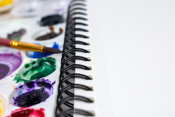 Close up view of a spiral bound notebook of watercolor paper.  Watercolor paints blurred in the...