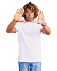 Fototapeta premium Young hispanic man wearing casual white tshirt doing frame using hands palms and fingers, camera perspective