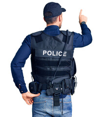 Young handsome man wearing police uniform posing backwards pointing ahead with finger hand