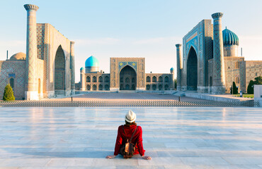 tourist woman with hat and dress red sitting on Registan, an old public square in the heart of the ancient city of Samarkand, Uzbekistan.