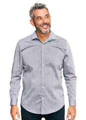Middle age grey-haired man wearing casual clothes looking away to side with smile on face, natural expression. laughing confident.