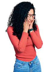 Young hispanic woman with curly hair wearing glasses rubbing eyes for fatigue and headache, sleepy...