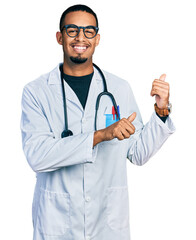 Young african american man wearing doctor uniform and stethoscope pointing to the back behind with...