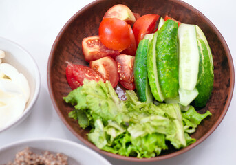 Dinner on the kitchen table, vegetarian green salad in a plate. Healthy fiber foods. Sliced cucumbers with tomatoes and herbs