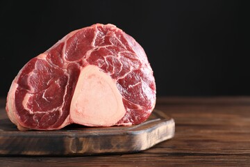 Piece of raw beef meat on wooden table against black background, closeup. Space for text