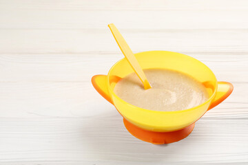 Baby food. Puree and spoon in bowl on white wooden table. Space for text