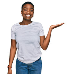 Young african american woman wearing casual white t shirt smiling cheerful presenting and pointing with palm of hand looking at the camera.