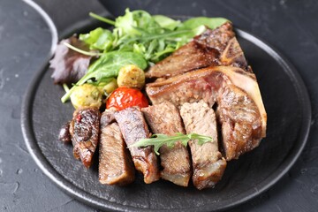 Delicious grilled beef meat, vegetables and greens on black table, closeup