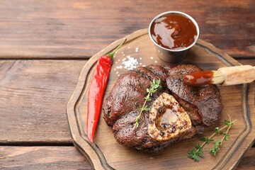 Delicious roasted beef meat served with sauce and spices on wooden table. Space for text
