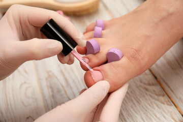Obraz na płótnie Canvas Professional pedicurist painting client`s toenails with polish in beauty salon, closeup