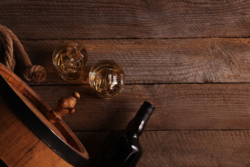 Whiskey with ice cubes in glasses, bottle and barrel on wooden table, flat lay. Space for text