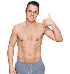 Fototapeta premium Handsome young man wearing swimwear shirtless smiling doing phone gesture with hand and fingers like talking on the telephone. communicating concepts.