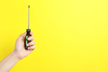 Woman holding screwdriver on yellow background, closeup. Space for text