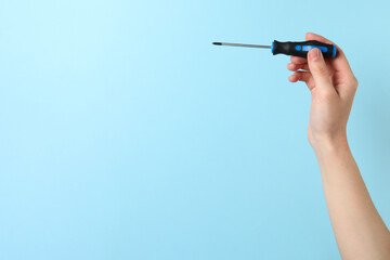 Woman holding screwdriver on light blue background, closeup. Space for text