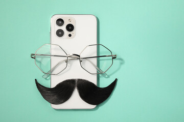 Artificial moustache, smartphone and glasses on turquoise background, top view. Space for text