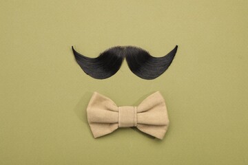 Artificial moustache and bow tie on khaki background, top view