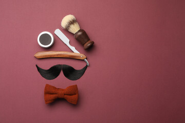 Artificial moustache and barber tools on burgundy background, flat lay. Space for text
