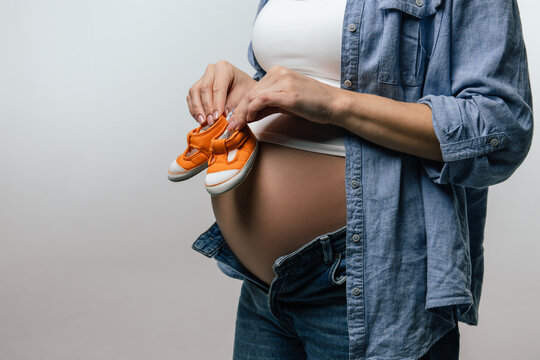 Pregnant woman with big belly showing orange cute baby shoes