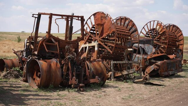 Desolate field with burnt agricultural machinery. Large metal structures of agricultural machinery damaged by fire. Concept of war, destruction, loss