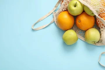 Foto op Canvas String bag with fresh apples and oranges on light blue background, top view. Space for text © New Africa
