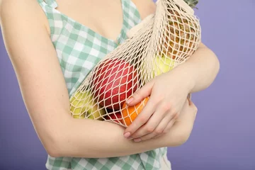 Foto op Plexiglas Woman with string bag of fresh fruits on violet background, closeup © New Africa