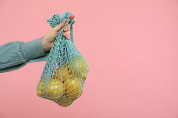 Foto op Plexiglas Woman with string bag of fresh lemons on pink background, closeup. Space for text © New Africa