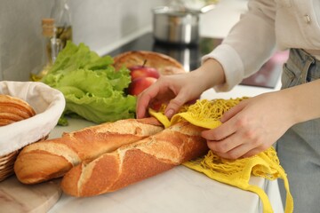 Woman taking baguettes out from string bag at countertop, closeup
