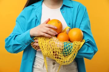 Foto op Plexiglas Woman with string bag of fresh oranges on orange background, closeup © New Africa