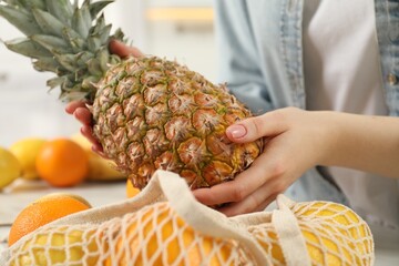 Woman taking pineapple out from string bag at table, closeup