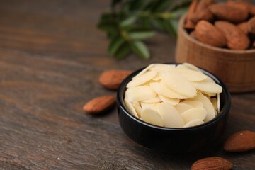 Fresh almond flakes in bowl and nuts on wooden table, closeup. Space for text