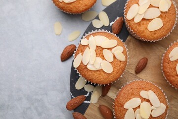 Muffins with fresh almond flakes and nuts on grey table, flat lay. Space for text