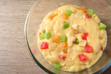 Raw dough with candied fruits in bowl on wooden table, top view
