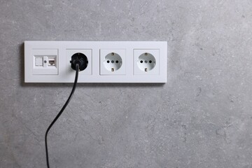 Power sockets and electric plug on grey wall, space for text