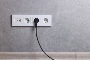 Power sockets and electric plug on grey wall, space for text - obrazy, fototapety, plakaty