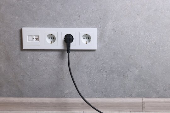 Power sockets and electric plug on grey wall, space for text