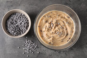 Raw dough with chocolate chips in bowl on grey table, flat lay
