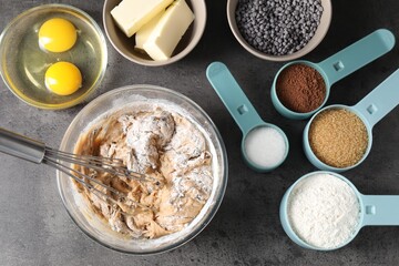Raw dough with chocolate chips in bowl and ingredients on grey table, flat lay