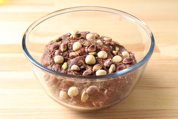 Raw chocolate dough with nuts in bowl on wooden table, closeup