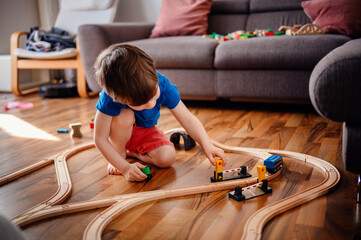 A little boy in blue deeply focused on navigating a toy train over the wooden tracks, embodying the...