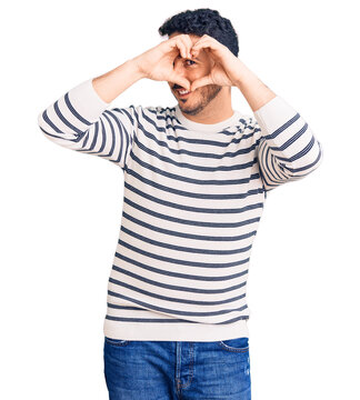 Young hispanic man wearing casual clothes doing heart shape with hand and fingers smiling looking through sign