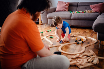 Engrossed in play, a young child sits on a wooden floor arranging a train track, highlighting a...