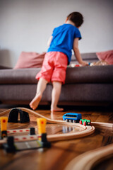 In a blur of motion, a child dashes around a wooden train set on the floor, showcasing dynamic play in a living room