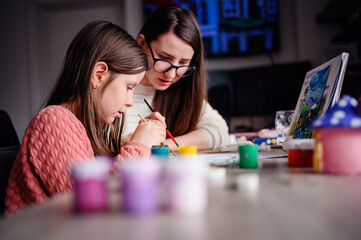 A young girl and a woman are immersed in painting, a nurturing moment highlighting the beauty of...