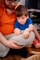 Fototapeta premium An adult and a young child explore a smartphone together, mixing the digital world with quality family time on the playroom floor