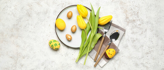 Table setting with Easter eggs, cutlery and tulip flowers on white grunge background