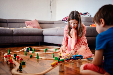 A girl and boy are deeply involved in setting up a sprawling wooden train track, showcasing...