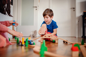 A young child deeply focused on playing with a wooden train set, constructing his own little world on the living room floor, showcasing early learning and creativity